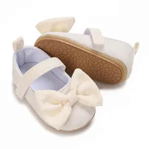 Nahaufnahme weißer Baby-Prinzessinnenschuhe mit großer Schleife und weicher brauner Sohle.