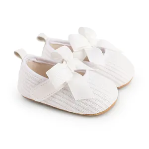 Gros plan sur des chaussures de cérémonie blanches pour bébé avec un grand nœud doux.