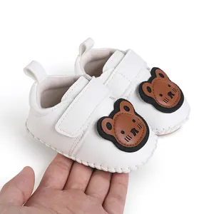 Detailansicht weißer Lauflernschuhe für Babys mit Bären-Aufnäher, in der Hand