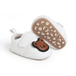 Detail von weichen weißen Babyschuhen mit Bärenmotiv und rutschfester Gummisohle