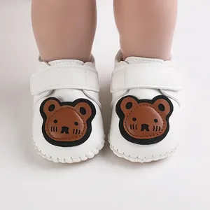 Frontale Nahaufnahme weißer Lauflernschuhe für Babys mit süßem braunem Bären-Aufnäher