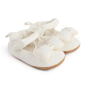 Détail de chaussures pour bébé crème avec tissu texturé et nœud en tulle élégant.