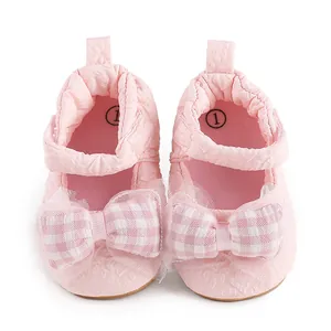 Vue détaillée de chaussures de marche pour bébé roses avec nœuds à carreaux et tissu gaufré.