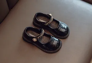 Detailansicht schwarzer Lackleder-Mary-Janes für Mädchen mit Goldkette und Perle.