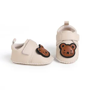 Nahaufnahme von beigen Babyschuhen mit einem niedlichen Bären-Cartoon-Patch-Detail