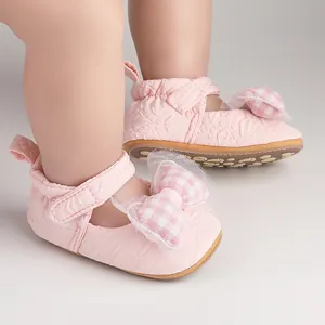 Gros plan de chaussures de marche roses pour bébé avec nœud à carreaux et détails en tulle.