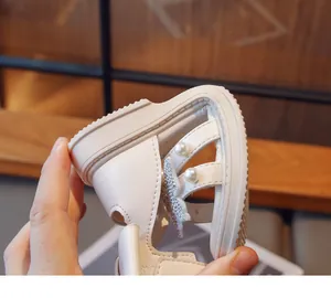 Close-up of girls' soft-soled white sandal with pearl and rhinestone butterfly detail.