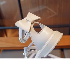 Detailed view of white girls sandals featuring an elegant bow and pearl accents