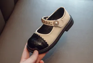 Detailansicht der zweifarbigen Mädchen-Mary-Janes mit Perlenschnalle und goldener Kette.