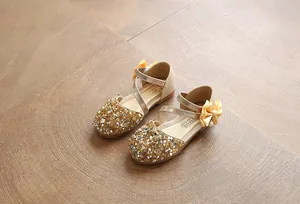 Close-up of gold sequin children's shoes with elegant yellow ribbon bows and pearls.