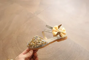 Detailed view of a shiny gold sequin girl's shoe with a satin bow and pearl charm.