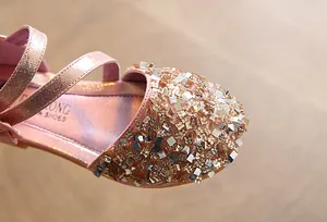 Close-up of rose gold girl's flats with shimmering square sequins and metallic straps.