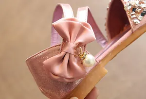 Close-up of children's pink sequin shoe with elegant satin bow and pearl pendant.