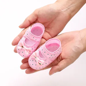 Detailed close-up view of soft pink polka dot baby shoes with bows held in hands