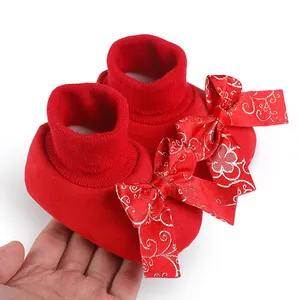 Detail of festive red baby walking shoes featuring a large gold embroidered bow
