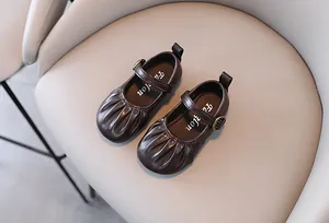 Dettaglio di scarpe Mary Jane marrone scuro per bambine con pieghe e cinturino fibbia.