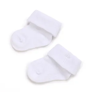 Close-up view of white knitted baby socks featuring an elegant embroidered cross on the cuff