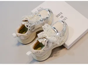 Detailed view of silver kids sneakers with delicate lace bows and pearl accents