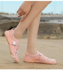 Close-up view of pink breathable mesh water shoes worn by a person on a sandy beach