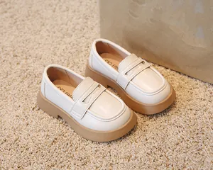 Mocassins pour enfants de couleur crème avec semelle marron sur un tapis doux