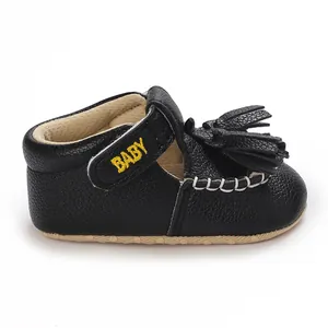Nahaufnahme von schwarzen Baby-Ledersandalen mit Troddeln und BABY-Stickerei am Riemen