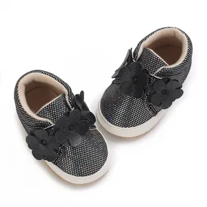 Gros plan de baskets bébé noires pailletées avec fleurs décoratives et semelles blanches