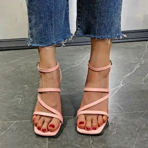 Nahaufnahme eleganter hellrosa Sandaletten mit Blockabsatz und eckiger Zehenpartie zur Jeans.