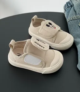 Primo piano di scarpe di tela beige per bambini con ricamo di Topolino e velcro.