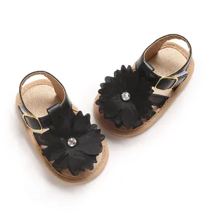 Detalle de sandalias negras para bebé con flor de tela y centro de cristal