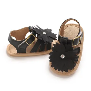 Detalle de sandalias negras para bebé con flores decorativas grandes y pedrería.