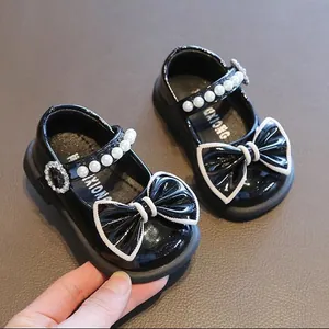 Detailansicht von schwarzen Lacklederschuhen für Babys mit Perlenriemen und Schleife.