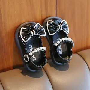 Nahaufnahme von schwarzen Lacklederschuhen für Babys mit großer Schleife und Perlen.
