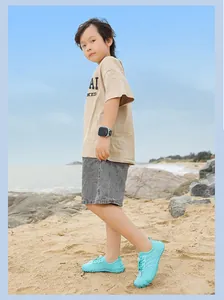 Junge trägt atmungsaktive Aqua-Schuhe, während er an einem sonnigen Sandstrand steht