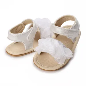 Dettaglio della decorazione floreale in pizzo bianco e cinturini argentati su sandali da neonata
