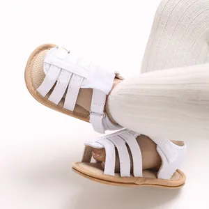 Dettaglio di sandali per neonati in tela bianca con suola morbida e chiusura velcro.