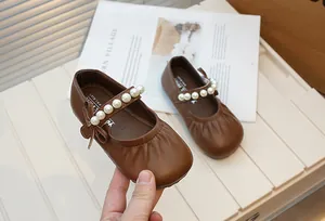 Detail of brown girls' Mary Jane shoes featuring an elegant pearl strap and bow.