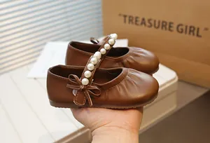 Close-up of brown Mary Jane girls shoes with pearl strap and bow detail.