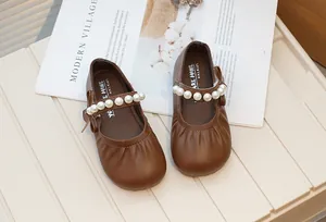 Detailed view of the elegant pearl strap and bow on these brown Mary Jane shoes.
