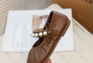 Close-up detail of brown Mary Jane girls shoe with elegant pearls and bow accent.