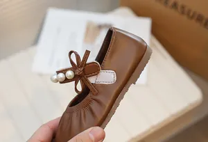 Brown retro Mary Jane girl's shoe with pearl buckle and bow detail, close-up view.