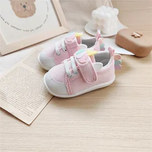 Soft-sole pink baby walking shoes with cute pastel cartoon wing decorations on a wooden table.