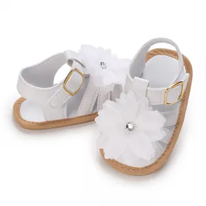 Detalle de sandalias blancas para bebé niña con una flor grande y suela blanda antideslizante.