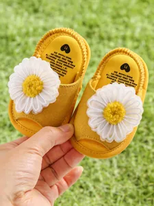 Vue détaillée de sandales jaunes pour bébé avec de grandes marguerites blanches sur herbe