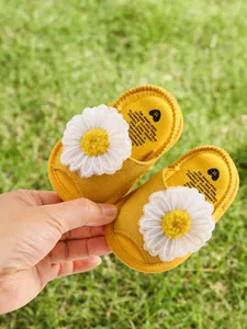 Gros plan sur la texture souple et la marguerite blanche de ces sandales jaunes bébé