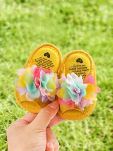 Gros plan de sandales jaunes pour bébé avec fleurs en tissu marguerite, tenues à la main