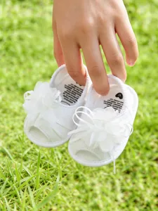 Vue rapprochée de sandales blanches pour bébé avec fleurs en maille sur herbe verte