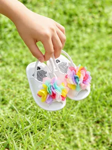 Gros plan de sandales blanches pour bébé avec fleurs en tissu colorées sur l'herbe