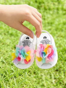 Détail de sandales blanches pour bébé avec fleurs en maille colorées sur l'herbe