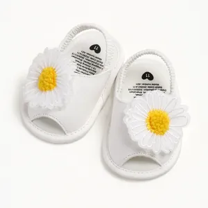 Détail de sandales blanches pour bébé avec applique de marguerite jaune et bride élastique