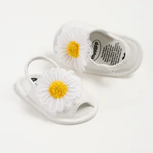 Gros plan de sandales blanches pour bébé avec une grande marguerite 3D décorative.